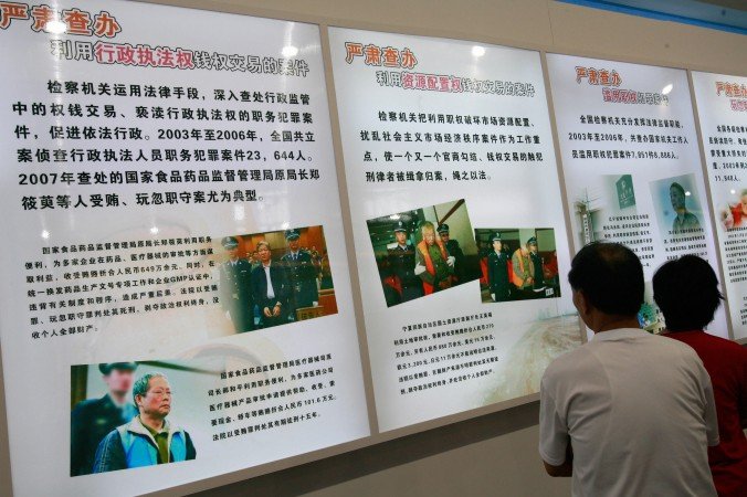 Visitors look at a billboard featuring alleged corrupt Chinese Communist Party members